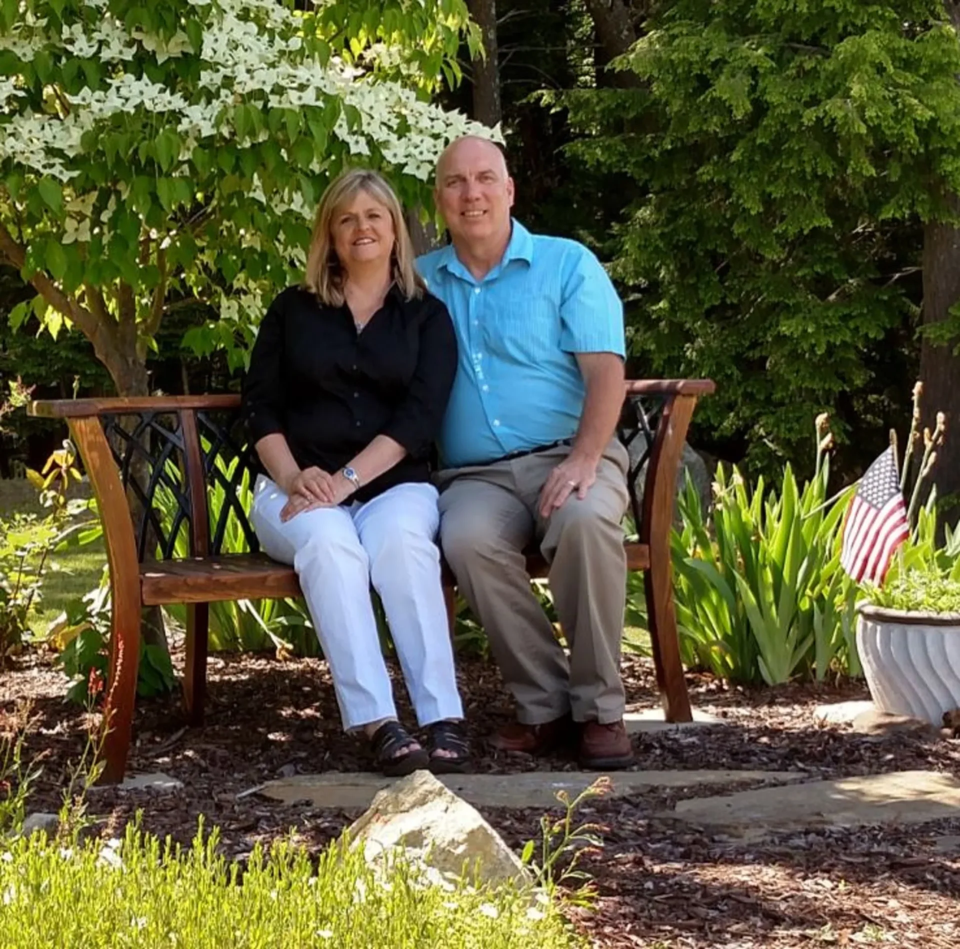 A man and woman sitting on a bench in the woods.