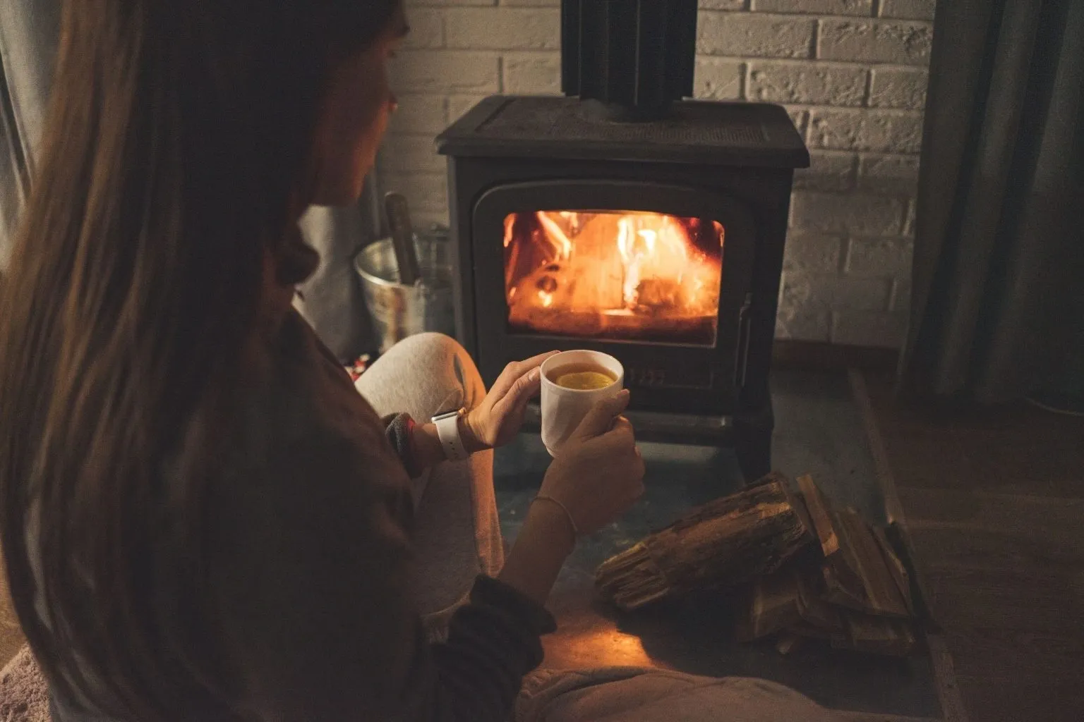 A person sitting in front of an open fire holding a cup.