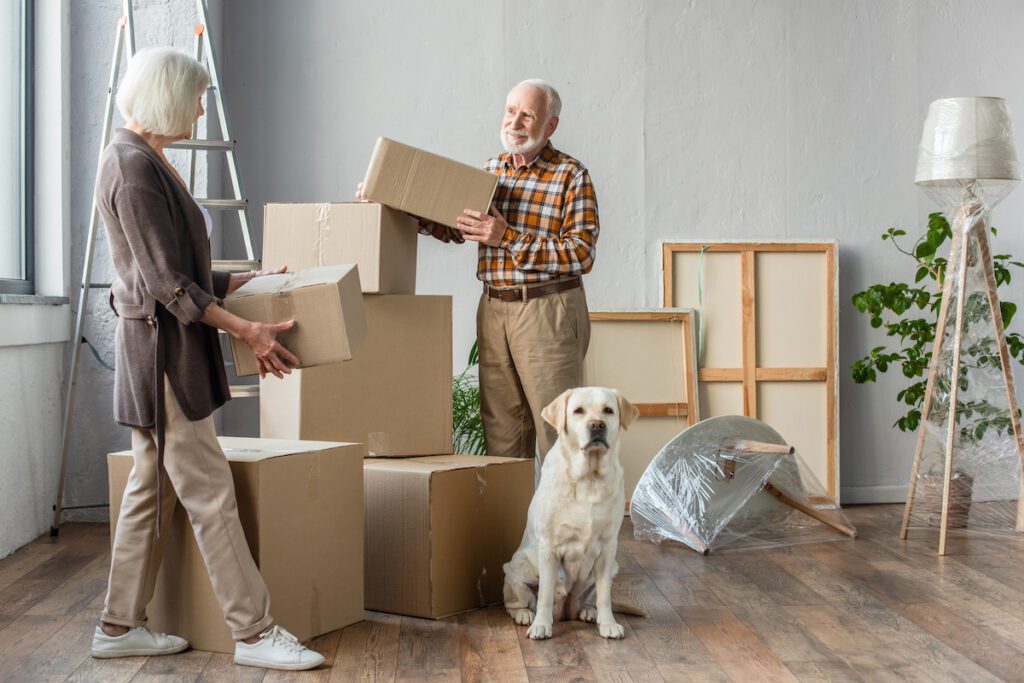 Elderly couple packing boxes with their dog nearby during a move.