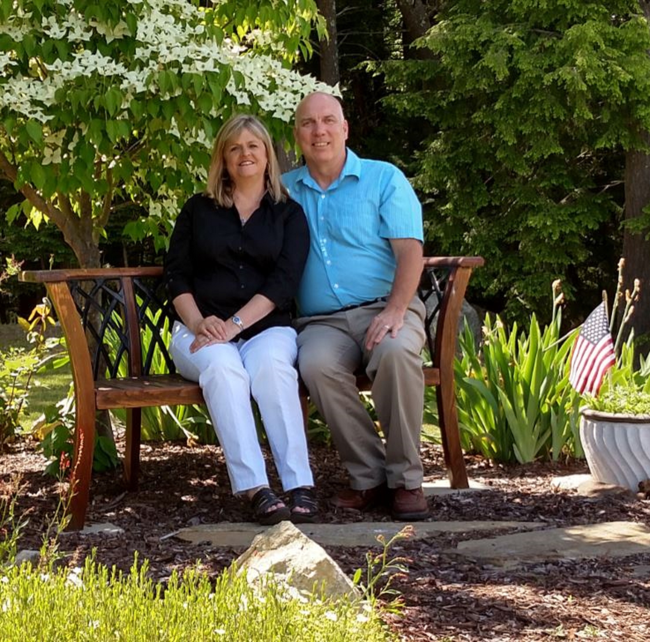 An elderly couple sitting on a wooden bench in a garden.