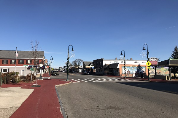 A street with a train passing through a small town under a clear blue sky.