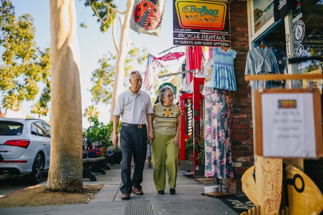 Elderly couple walking together in a vibrant market street filled with colorful clothes.