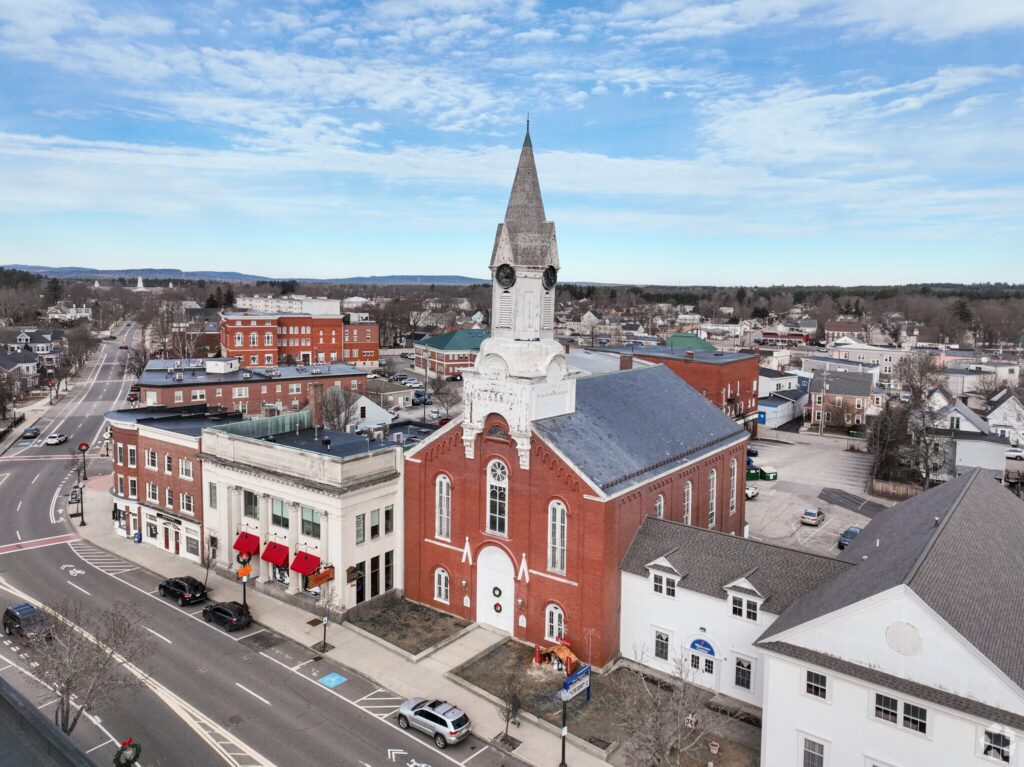 A historic red-brick church with a tall white steeple in a small town.