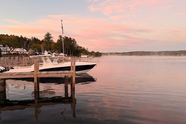 A calm lake at sunset with a boat docked by a wooden pier.