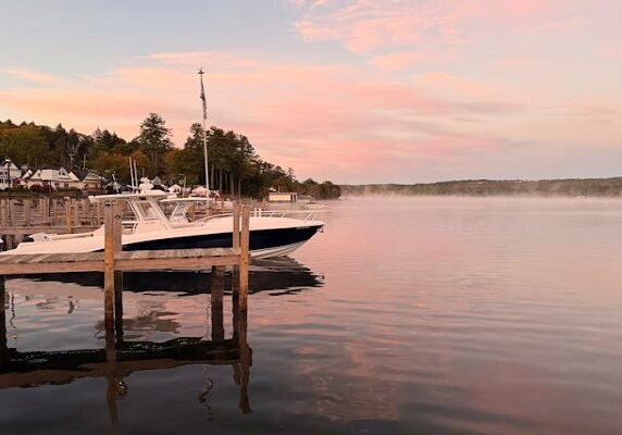 A calm lake at sunset with a boat docked by a wooden pier.