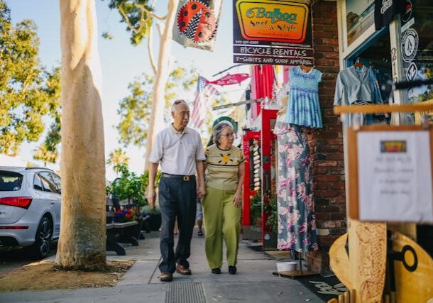 Elderly couple walking together in a vibrant market street filled with colorful clothes.