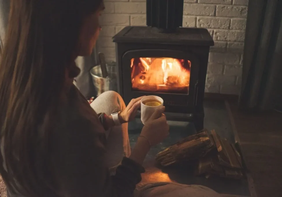 A person sitting in front of an open fire holding a cup.